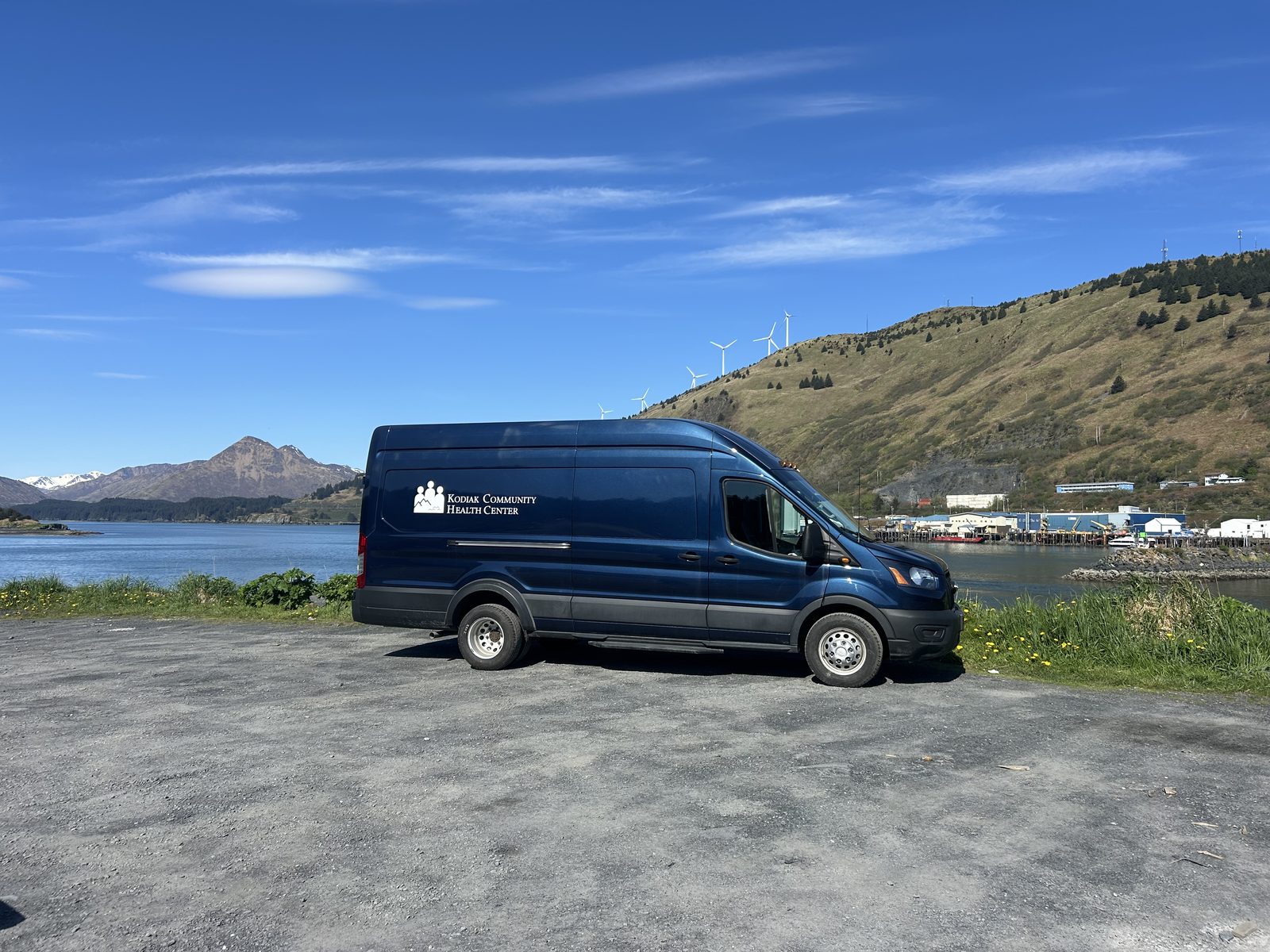 The mobile health unit parked beside the water outside Kodiak, with snow-capped mountains in the distance